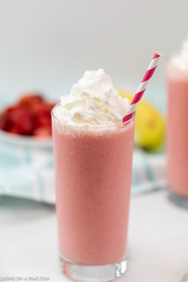 Strawberry Smoothie with whipped cream and straw in it with strawberries and lemons in the back ground.