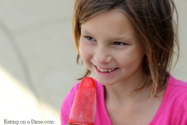A girl holding a red jello popsicles and smiling. 