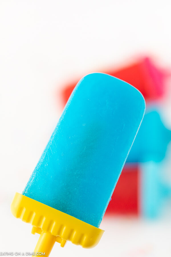 Close up of a blue jello popsicles with other popsicles in the back ground. 