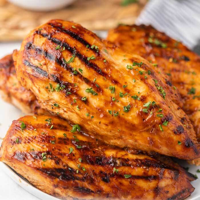 4 pieces of grilled barbecue chicken on a white plate topped with fresh parsley. 
