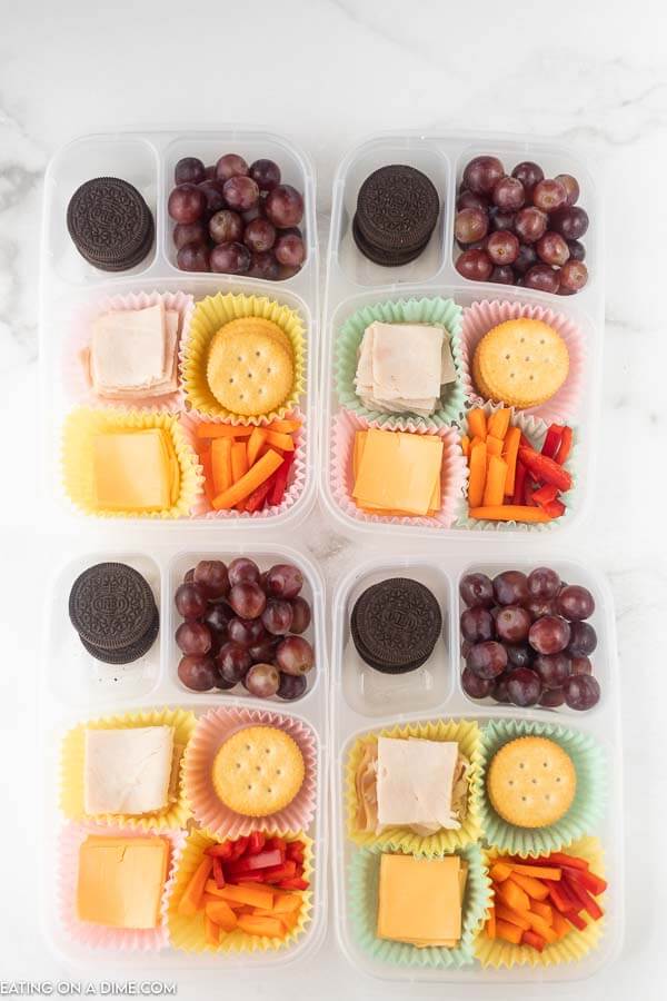 Close up of containers with meat, cheese, carrots, crackers, oreo, and grapes. 