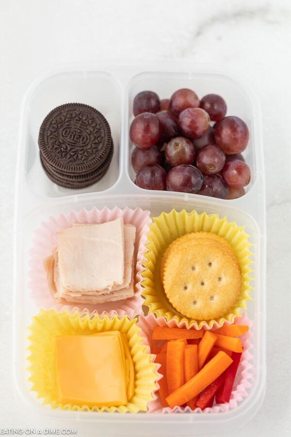 Close up image of a container with oreo, grapes, meat, cheese, crackers and carrots. 