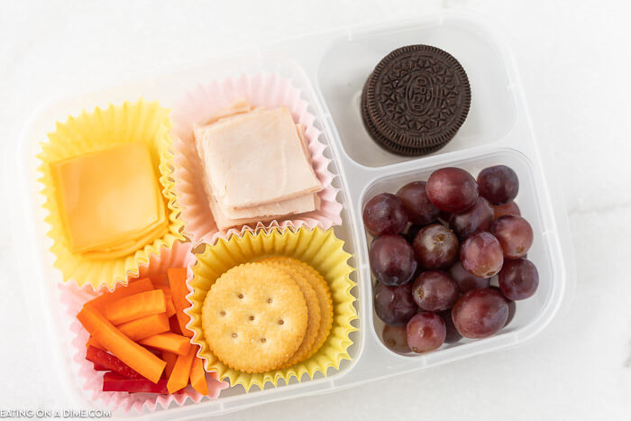 Close up image of container with meat, cheese, crackers, carrots, grapes, and oreo.