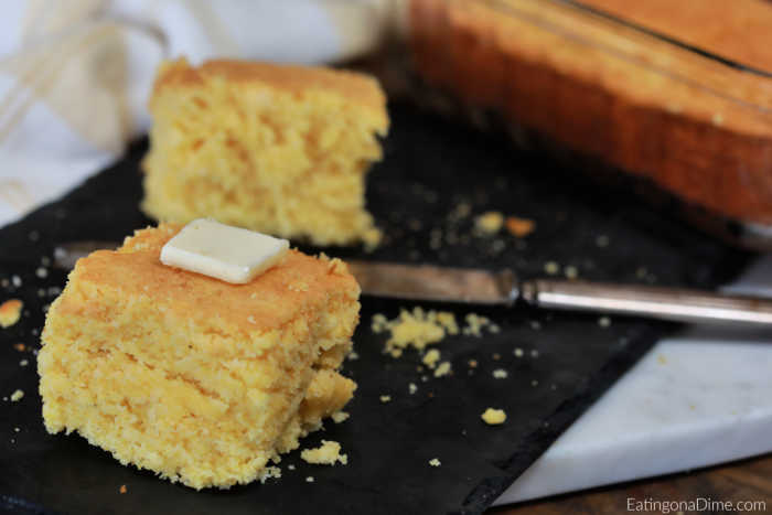 Close up image of cornbread on a napkin with a slice of butter on top. 