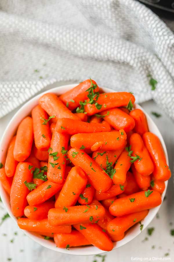 Glazed carrots in a white bowl topped with fresh parsley. 