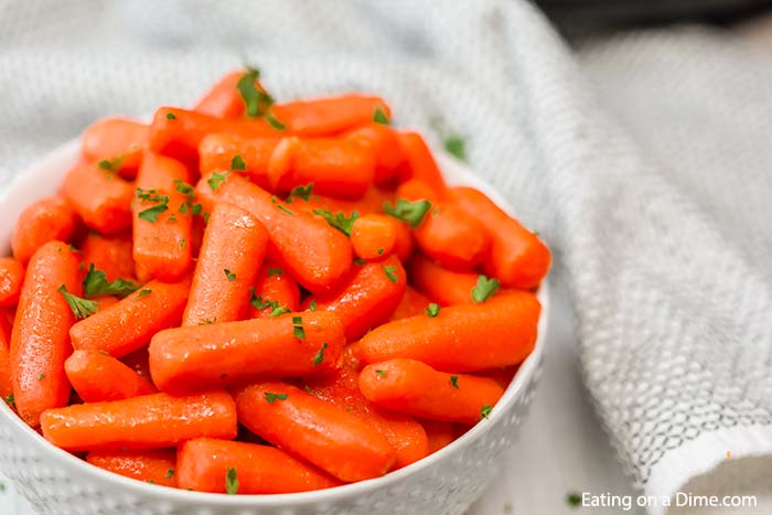 Glazed carrots in a white bowl topped with fresh chopped parsley. 