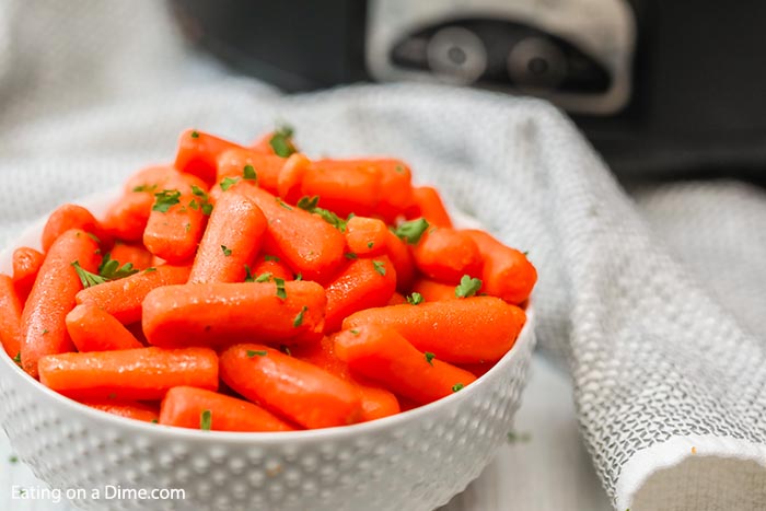 A bowl of glazed carrots in front of a crock pot. 