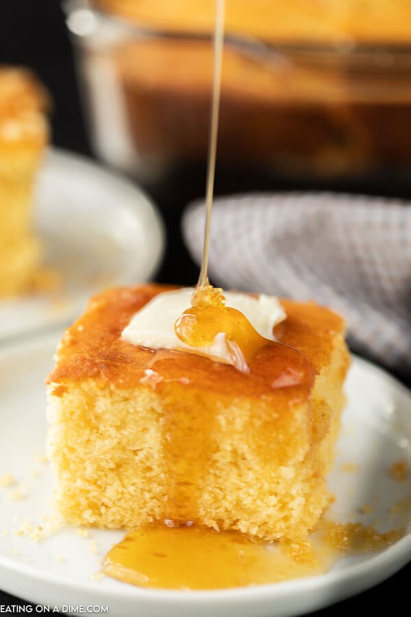 Close up image of a piece of cornbread with butter on top with syrup being drizzled on top. 