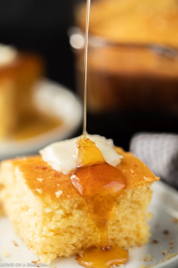 Close up image of a piece of cornbread with butter and syrup being drizzled on top.  