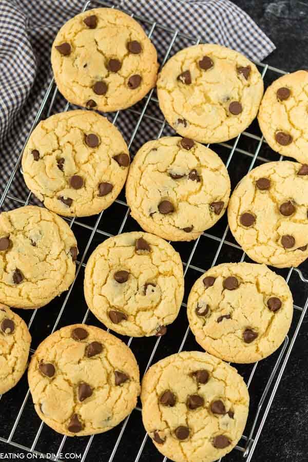 Chocolate chip cookies on a wire rack on a black countertop with a plaid linen in the back ground. 