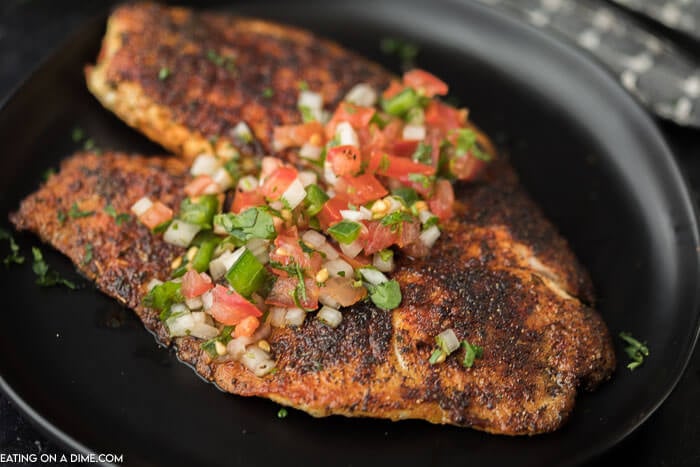 A blackened tilapia fillet on a black plate topped with pico 