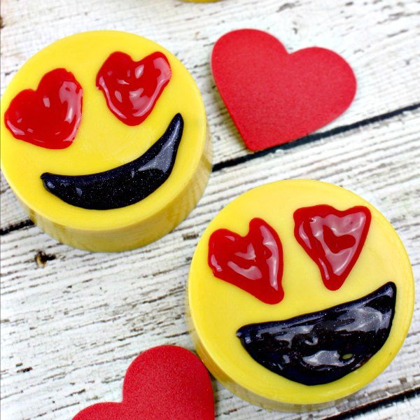 Emoji chocolate covered Oreos on a wooden board with red paper hearts next to it 