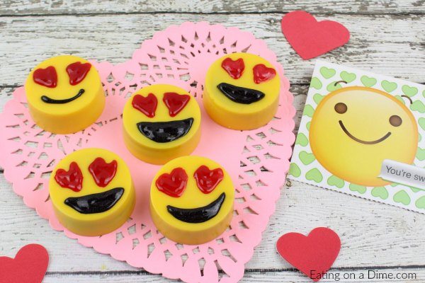 Emoji chocolate covered Oreos on a pink heart on a wooden board 