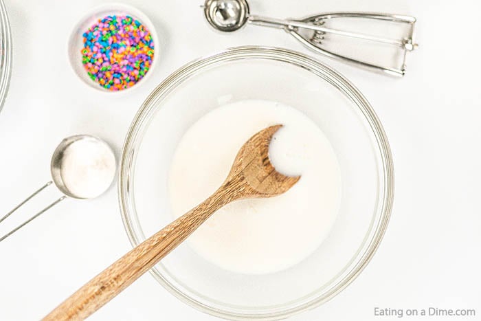 Close up image of a bowl of sprinkles, and ingredients being put in a clear bowl with a wooden spoon. 