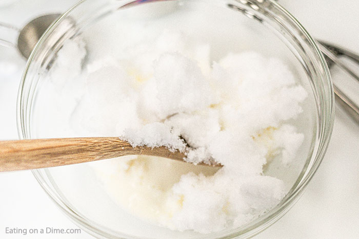 Close up image of snow ice cream being mixed in a clear bowl with a wooden spoon.