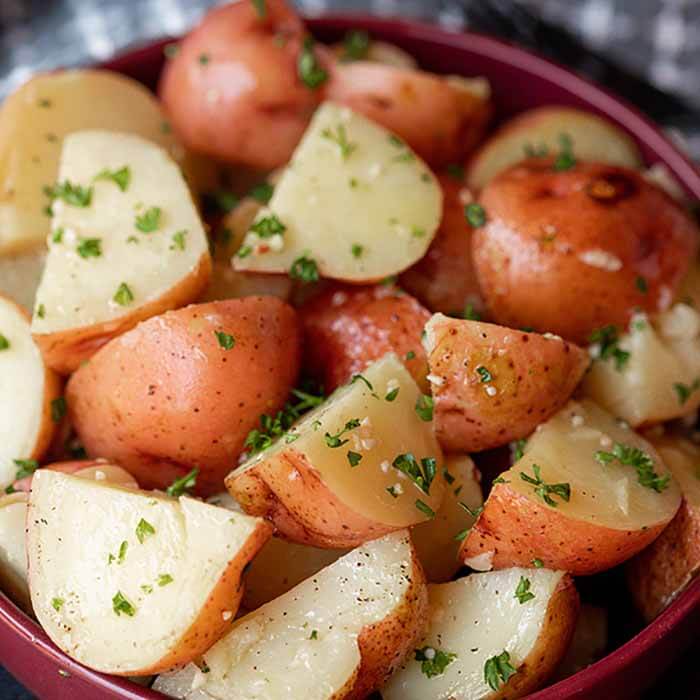 Close up of cooked instant pot red potatoes in a large red bowl topped with fresh parsley.  