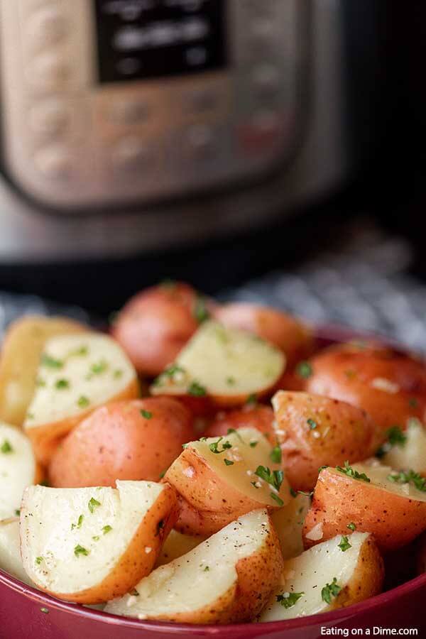 Cooked instant pot red potatoes in a large red bowl topped with fresh parsley with the instant pot behind it. 
