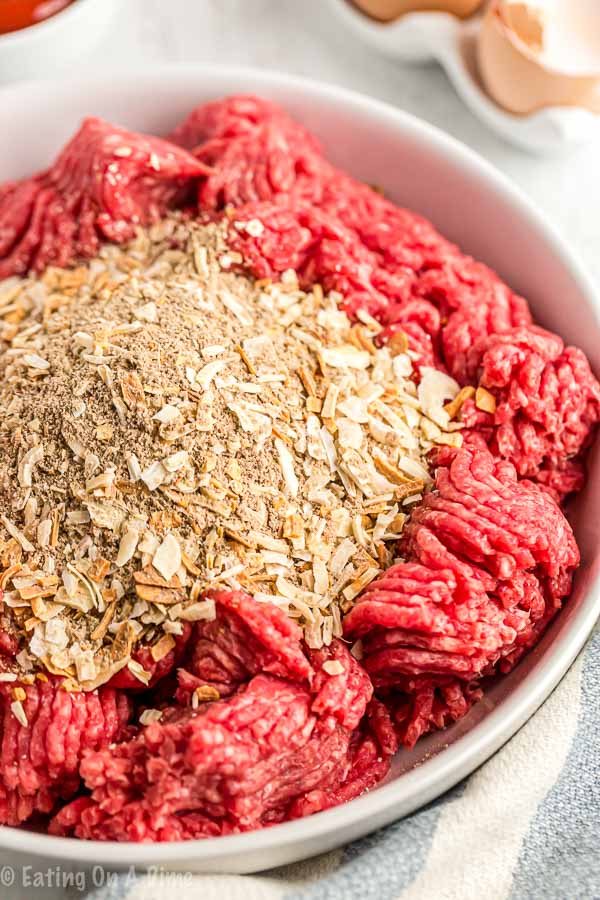 Adding ground beef to a bowl and mixing in egg, oats, soup mix and ketchup