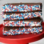 Three ice cream sandwiches coated with red, white, and blue star-shaped sprinkles are stacked on a red cake stand—perfect for your 4th of July Ice Cream Sandwich Recipe celebration.