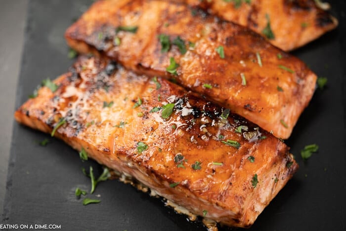 3 pieces of cooked salmon on a black platter topped with parsley with the honey glaze on top 