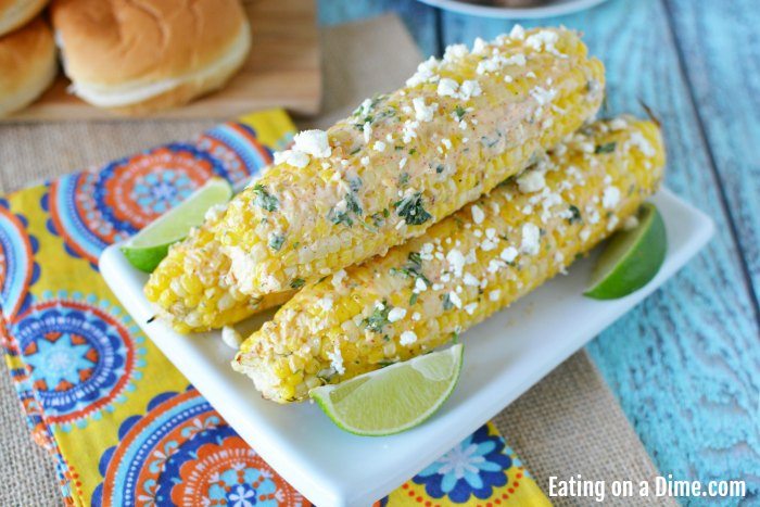 Close up image of Mexican Corn on the Cob on a white plate with lime wedges. 