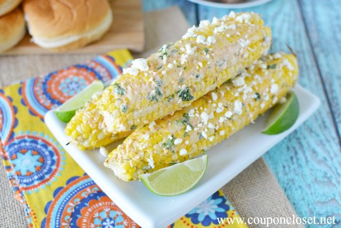 Close up image of Mexican Corn on the Cob on a white plate with a side of lime wedges. 