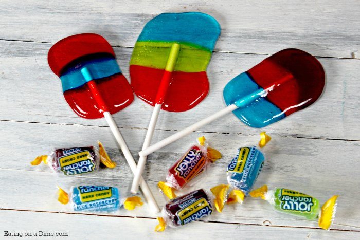 3 jolly ranch suckers laying on a wooden table with jolly ranchers scattered around it.  
