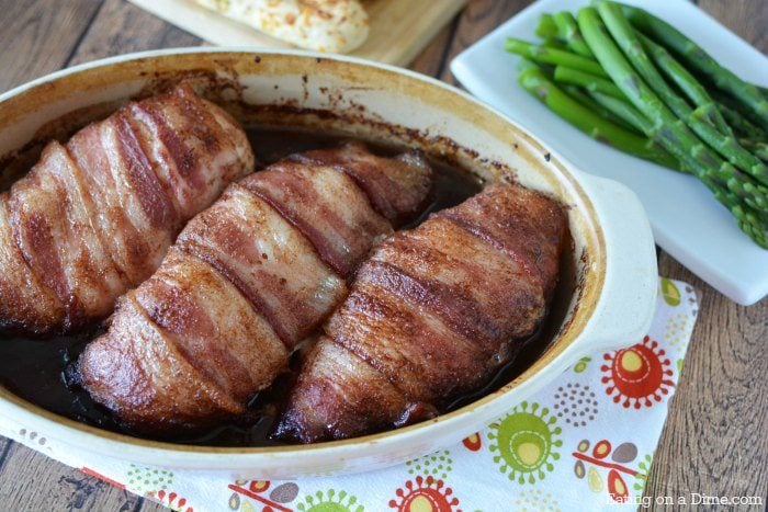 Close up image of bacon wrapped chicken in a baking dish with a side of asparagus