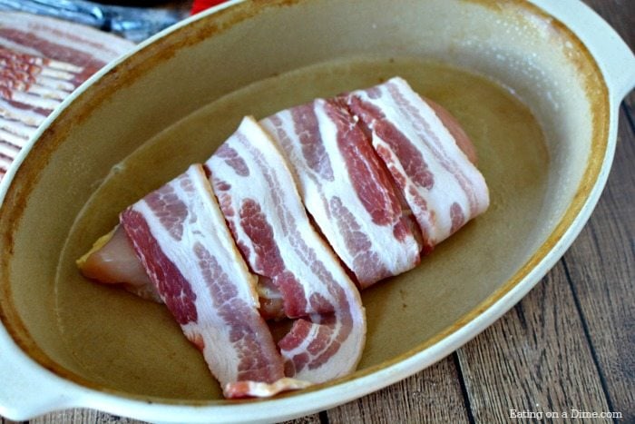 close up image of chicken being wrapped in bacon in a baking dish. 