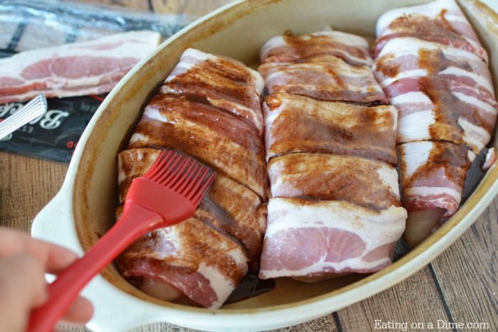 close up image of chicken wrapped in bacon and seasoning being brushed on. 