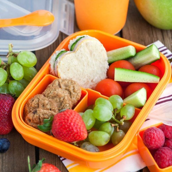 bento lunch container with vegetables, fruit, cookies and heart shaped sandwich. 