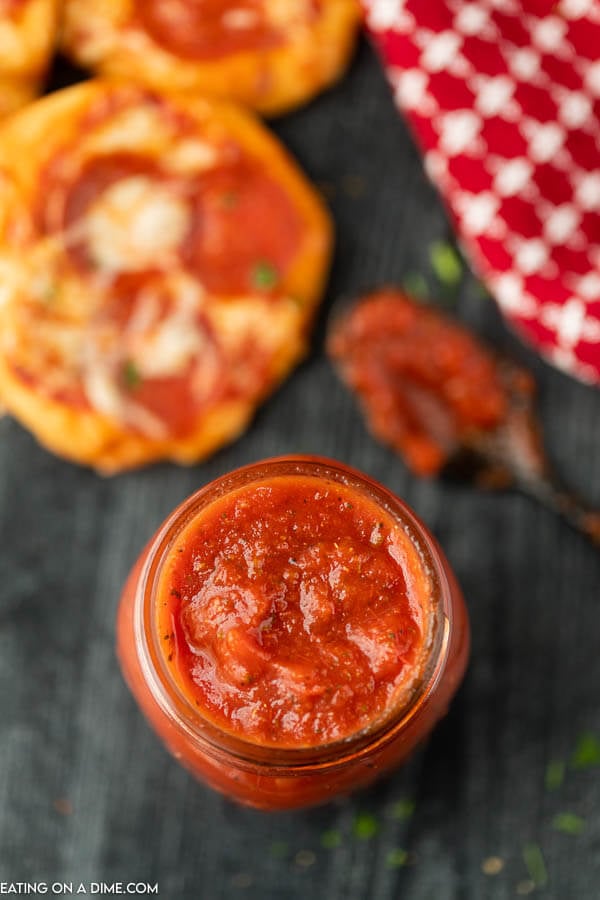 The top of a mason jar filled with pizza sauce and a messy spoon in the back ground. 