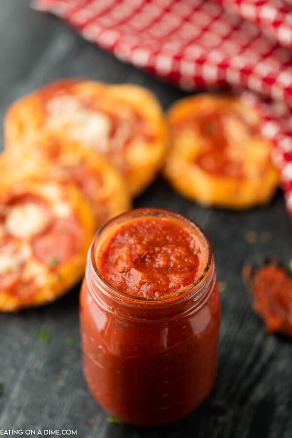 Pizza sauce in a mason jar with mini pizzas in the back ground 