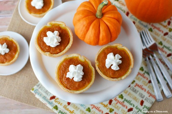 3 mini pumpkin pies on a cake stand with other mini pumpkin pies around it 