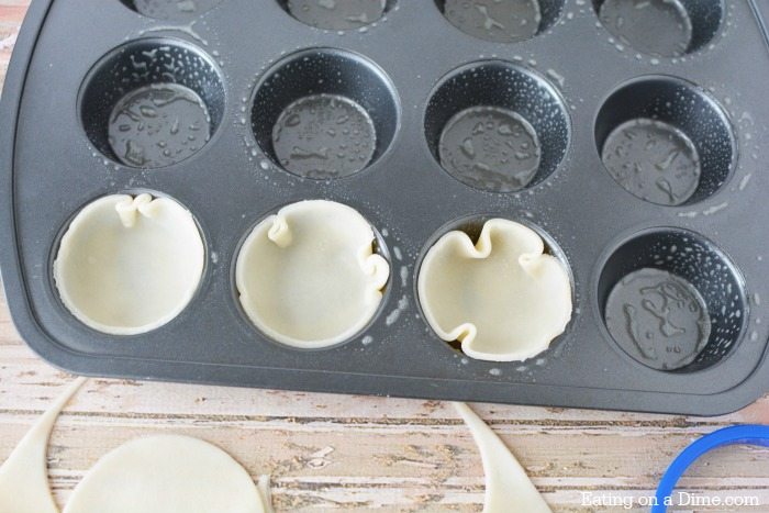 The pie crusts being pressed into a muffin tin 