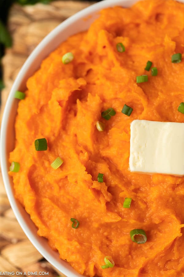 Closeup picture of  mashed sweet potatoes in white bowl with butter on top.