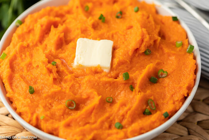 Closeup picture of  mashed sweet potatoes in white bowl with butter on top.