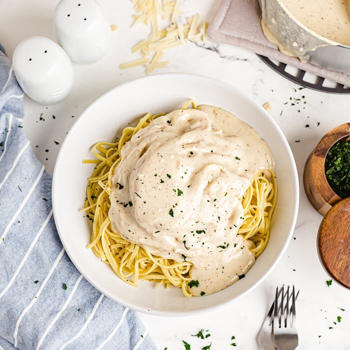 A bowl of fettuccine noodles topped with Alfredo sauce and fresh parsely. 