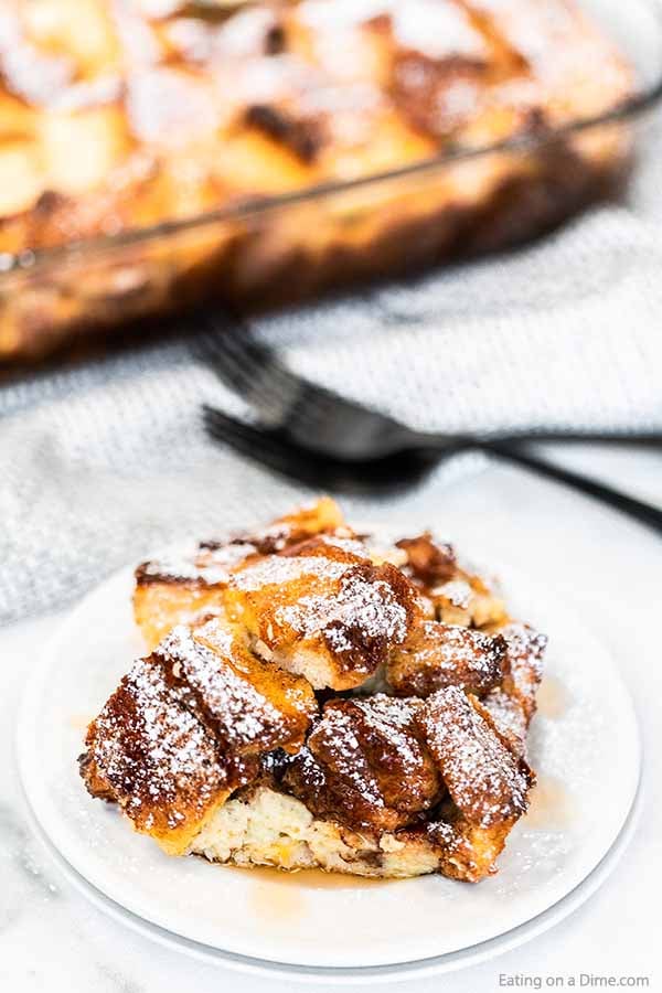 French toast casserole recipe is a delicious overnight breakfast casserole. This recipe is simple enough for busy mornings but perfect for guests. Close up image of a serving of french toast casserole on a white plate with two forks.