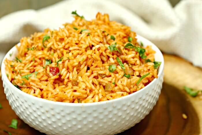 A white bowl full of Spanish Rice topped with fresh cilantro on a wooden platter. 