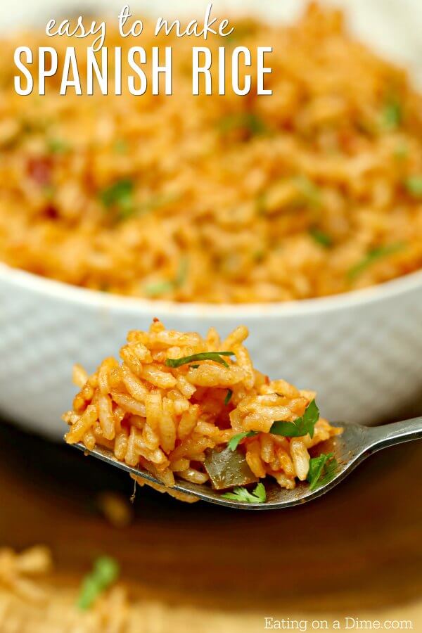 A fork with Spanish rice on it with a large bowl of Spanish rice behind it. 
