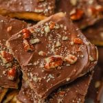 Close-up of Saltine Cracker Toffee squares coated in glossy chocolate and topped with chopped pecans, stacked together. The smooth surface glistens, with nut pieces generously sprinkled on top.