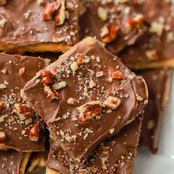 Close-up of Saltine Cracker Toffee bars topped with chopped pecans, showing a smooth chocolate layer and scattered nut pieces on square-shaped treats.