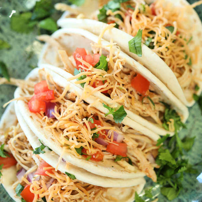 Chicken Tacos on a plate topped with tomatoes, cheese and lettuce