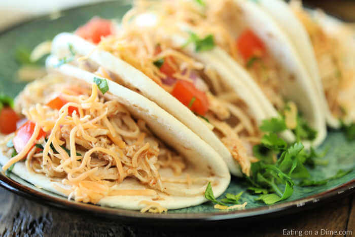 Crockpot Chicken Tacos recipe is so easy! It's very tasty and sure to make dinner a breeze. Crockpot Chicken tacos has only 3 ingredients and will be a hit. Chicken Tacos on a plate topped with tomatoes, cheese and lettuce