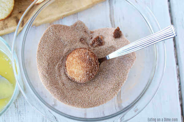Close up image of mini donut muffins rolled in cinnamon sugar mixture in a clear bowl with a spoon. 