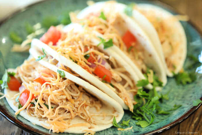 Chicken Tacos on a plate topped with tomatoes, cheese and lettuce