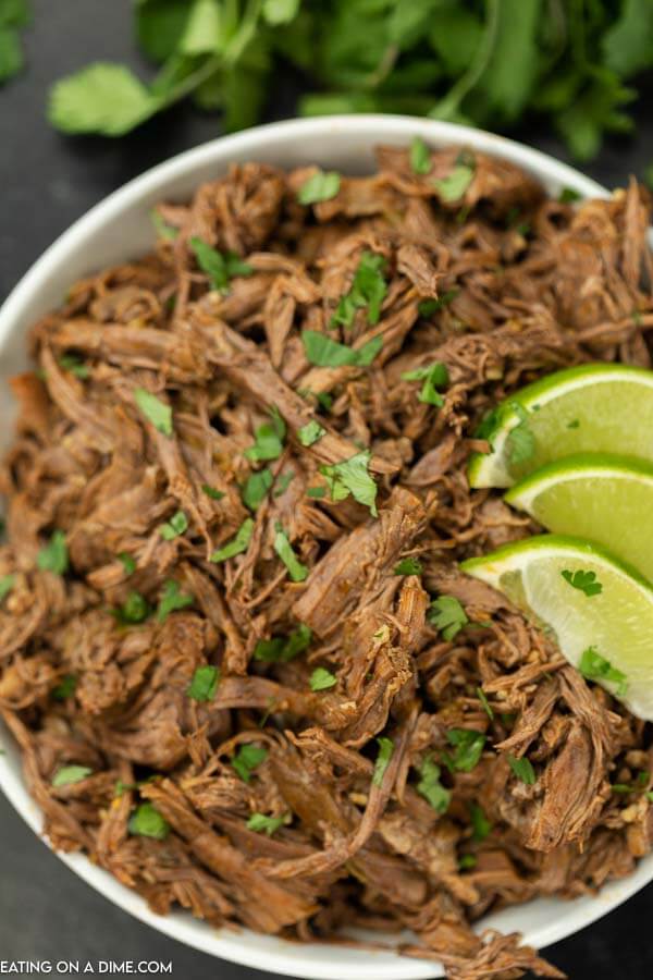 A large bowl of Mexican Shredded Beef topped with cilantro and limes. 