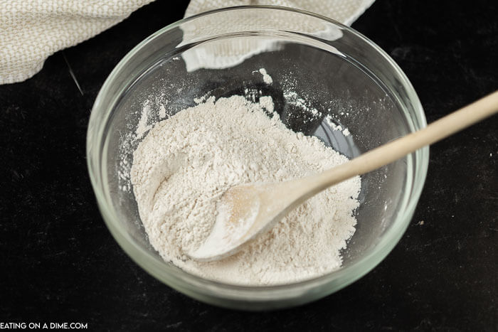 Close up image of a clear bowl of flour with a spoon 