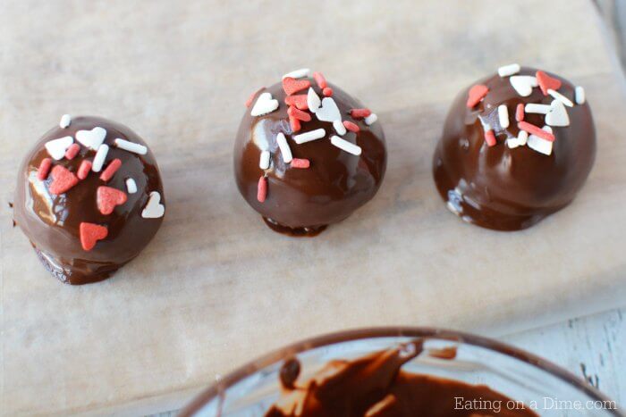The cake balls dipped in milk chocolate, placed on a baking sheet and topped with Valentine's Day sprinkles 